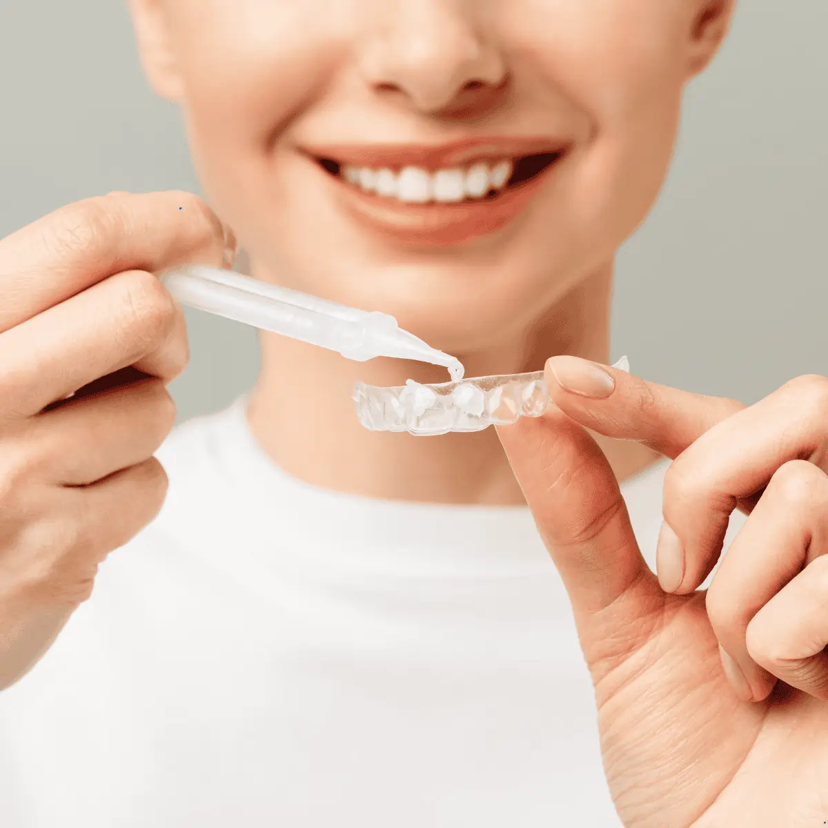 Personne souriante déposant du gel dans une gouttière dentaire transparente.