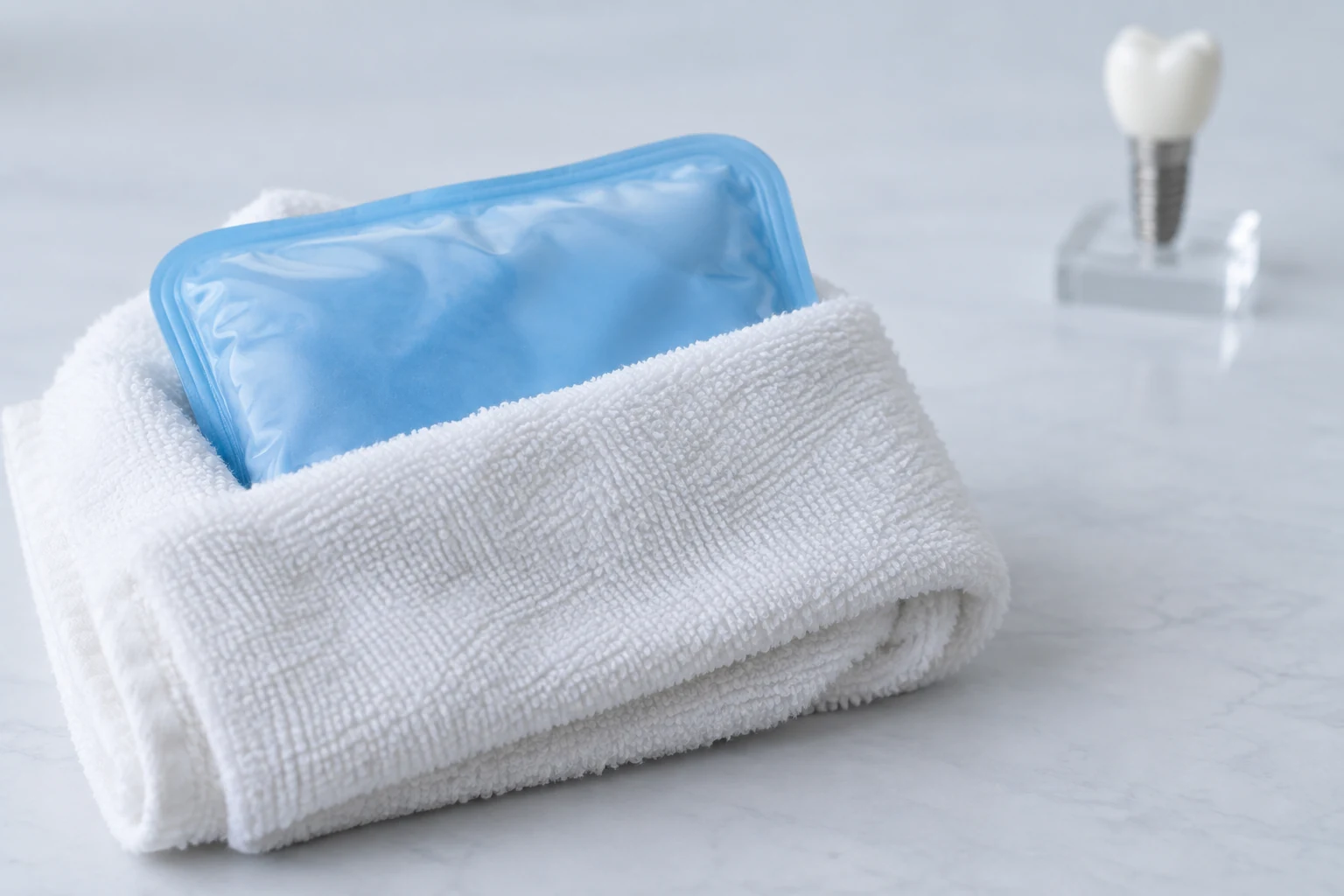 Poche froide réutilisable enveloppée dans une serviette blanche, avec un modèle d’implant en arrière-plan.