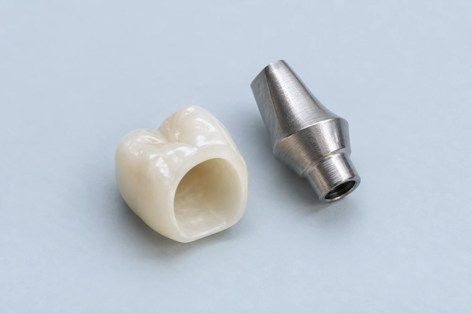Couronne dentaire et pilier en titane séparés, avec leurs surfaces de connexion visibles.